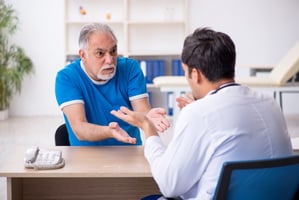 older man in blue shirt gesturing angrily to a male doctor